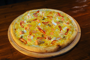 Italian pizza with fish and cheese, with red hot pepper on a wooden table