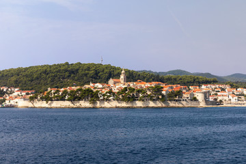 Fototapeta premium Korcula island with the old city walls, view from the sea on a sunny day in the summer. Blue adriatic sea, the south mediterranean coast of Croatia Europe. Beautiful landscape with greenery