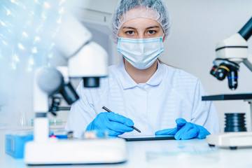 Little girl in science class with microscope on the table. Little girl scientist writing in notebook