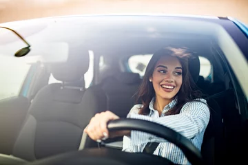 Foto op Canvas Happy woman driving a car and smiling. Cute young success happy brunette woman is driving a car. Portrait of happy female driver steering car with safety belt © Dragana Gordic