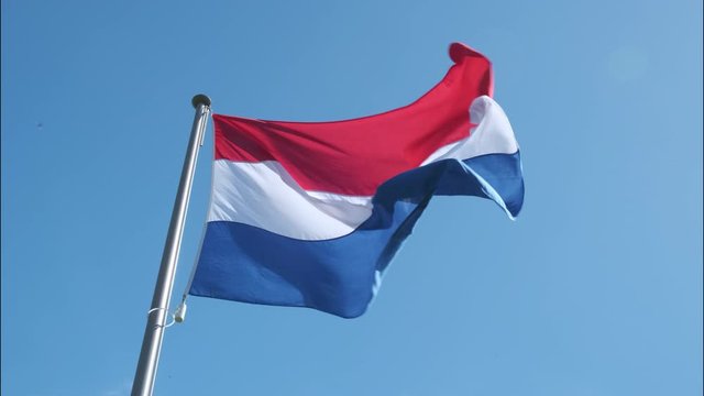 Dutch red, white and blue flag waving in the wind with a blue sky in the background during a sunny day. Slow motion clip.