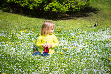 cute little girl with flowers looking at butterfly in spring nature