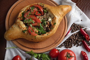 Georgian khachapuri with meat and tomatoes on a round kitchen board top view

