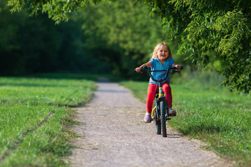 cute happy little girl riding bike in nature