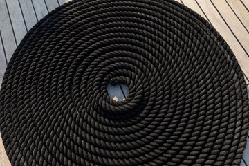 Black rope in the shape of a coil on board of a boat laying on the deck. Made into a beautiful traditional loop twist to secure the cord and creating a neat design decoration.