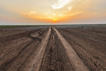 Fototapeta na wymiar Dirt road in the parched lake with sunset sky