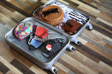 Suitcase with women clothes and cotton face mask on wooden floor background. Preparing for trip abroad after corona virus pandemic. Travel concept.