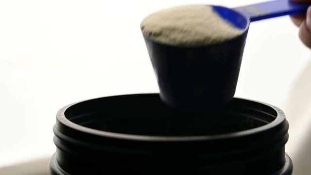 Sports nutrition protein is scooped with a measuring spoon from a jar