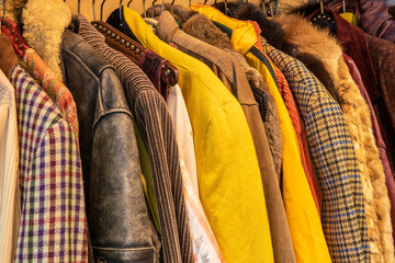 Sideview of colorful yellow and brown tinted vintage clothes, jackets with different patterns, colors and textures hanging on a rack. Recylcing clothing, circularity