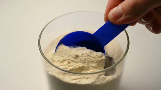 Sports nutrition protein is scooped with a measuring spoon from a jar