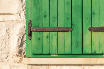 Close up of the exterior of  green painted closed wooden barn window blinds with metal details and the light colored limestone wall with big stone pieces. Typical mediterranean style architecture