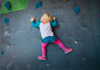 Fototapeta premium Little girl climbing on artificial boulders wall in gym