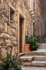 Fototapeta na wymiar Narrow old Mediterranean street with stairs in Korcula. Rough stone houses and facades, green plants, flowers in Dalmatia, Croatia. Historical place creating a picturesque and idyllic scenery