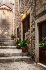 Fototapeta na wymiar Korcula old narrow Mediterranean street with stairs. Rough stone houses and facades, green plants, flowers in Dalmatia, Croatia. Historical place creating a picturesque and idyllic scenery