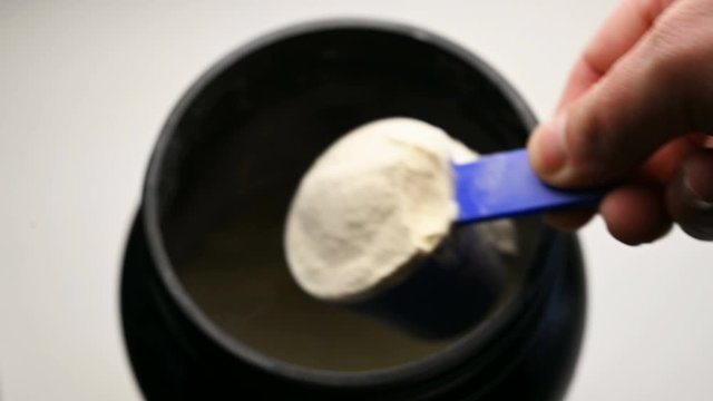 Sports nutrition protein is scooped with a measuring spoon from a jar