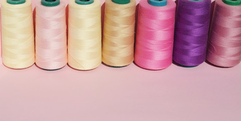 Sewing threads of different colors stand in a row on a pink background. Copy space Banner