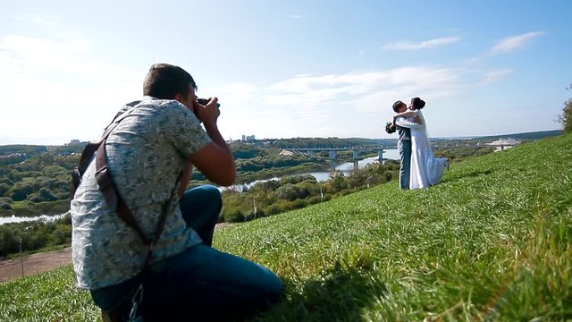 Wedding photographer taking pictures of the bride and groom on a hillside