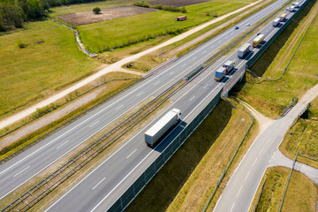 Aerial Follow Shot of White Semi Truck with Cargo Trailer Attached Moving Through Industrial Warehouse, Rural Area. Sun Shines and the Sky Are Blue.