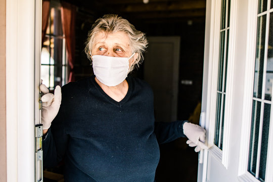 Elderly Woman, Grandma Wearing A Mask Standing At The Door Looking Outside.