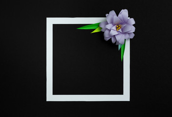 Square frame with lilac pastel color paper flower on black background. Flat lay, copy space, floral art