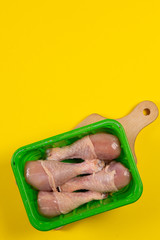 frozen chicken legs in a plastic container on yellow background