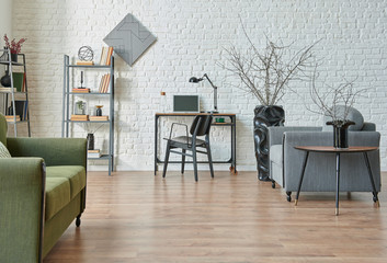 Modern white brick wall background, green and grey sofa, black furniture detail, working table with bookshelf.