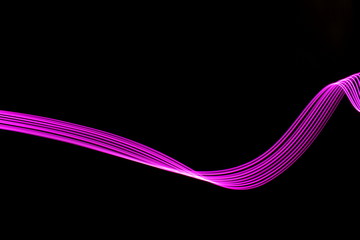 Long exposure photograph of neon pink colour in an abstract swirl, parallel lines pattern against a black background. Light painting photography.