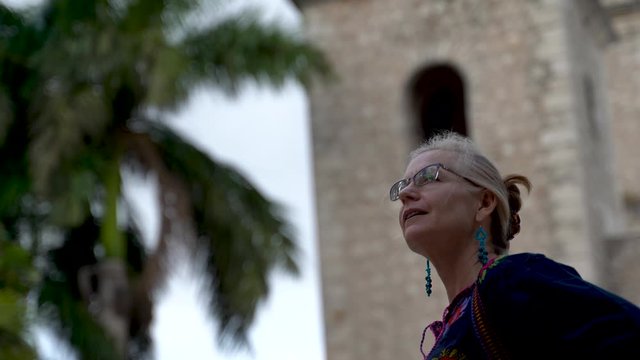 Beautiful blond middle aged mature woman smiles and looks up in the Hidalgo park in Merida, Museum.