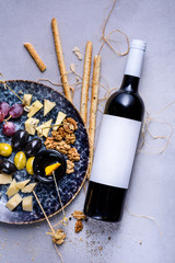 Cheese plate with grapes and olives. Snacks and cheese served with bottle of wine. Top view, copy space.