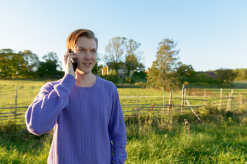 Happy young man talking on mobile phone in peaceful grassy plain with nature