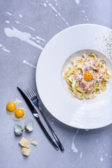 Pasta carbonara with quail egg, plate full of Italian tagliatelle with ham and cheese. Top view, grey background.