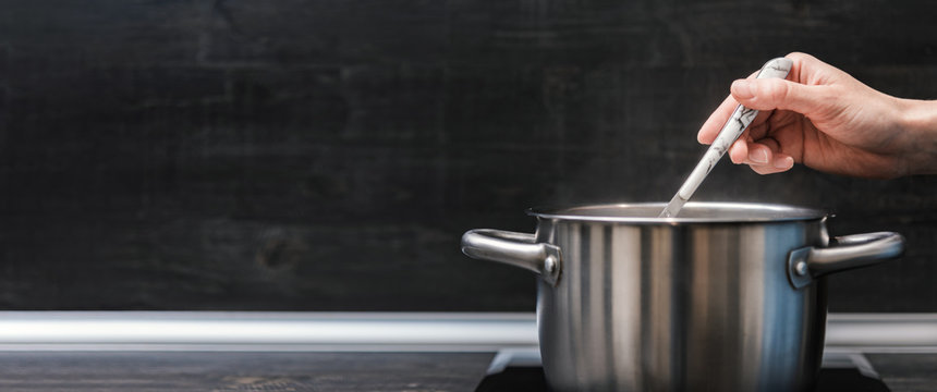 Hand with tablespoon mixing food in saucepan, copy space.