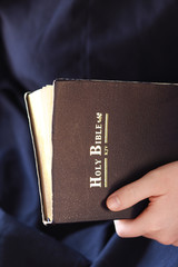 Hands holding an open Holly Bible on a dark background.