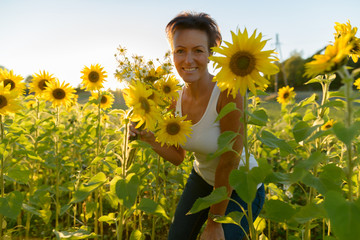 Happy mature beautiful woman holding flowers in the sunflower garden farm