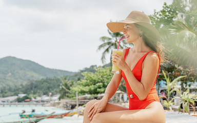 Young beautiful woman in a red swimsuit and a straw hat enjoying summer vacation, beach relax, summer in tropics.