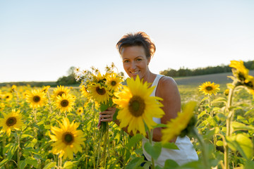 Fototapeta premium Happy mature beautiful woman holding flowers in the sunflower garden farm