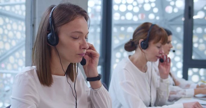 Close up of young Caucasian woman in headset talking with client in call center. Female operator of customer support office. Girl helping to solve technical problem online. Sells managers.