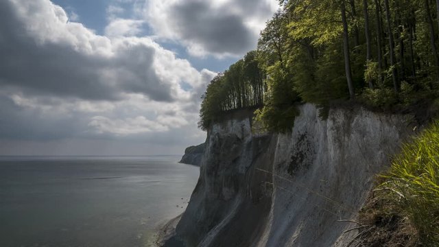 Time lapse of moving clouds next to the chalk cliffs on the German island Ruegen at the Jasmund National Park with trees in the forground 
