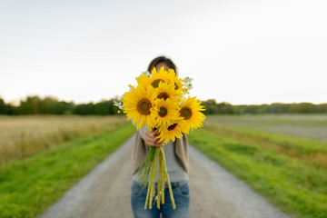 Young woman giving sunflowers against view of the field in nature