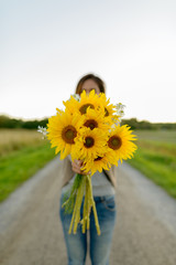 Young woman giving sunflowers against view of the field in nature