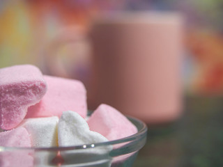 a bowl with pieces of white and pink marshmallows is on the green table. pink coffee cup on the background. close up. copy space