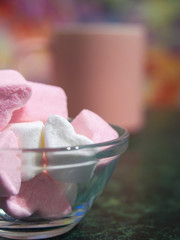 a bowl with pieces of white and pink marshmallows is on the green table. pink coffee cup on the background. close up. copy space