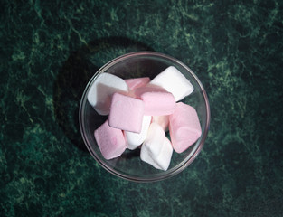 a bowl with pieces of white and pink marshmallows is on the green table. close up. copy space. top view.