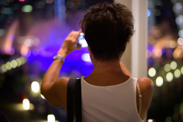 Rear view of mature tourist woman taking picture with phone in the city at night