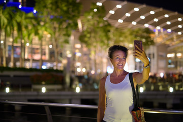 Happy mature beautiful tourist woman taking selfie in the city at night