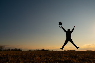 The contour of a man against the sky. The man jumped, stretching his arms and legs in the shape of a star. He has a bag in his hand. Joy concept