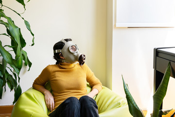Horizontal view of woman with gas mask surrounded with plants looking through the window. Conceptual idea of greenhouse effect in ecosystem. Quarantine at home and covid 19 coronavirus concept.
