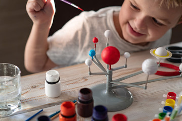 Boy tinkering a model of the solar system Concept of teaching children. Studying astronomy from childhood. Developing creativity from early age. Drawing with brushes and paints. Lockdown entertainment © Ekaterina
