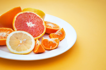 Fototapeta na wymiar Sweet citrus: lemon, tangerine, orange on a white plate on a yellow background