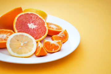 Sweet citrus: lemon, tangerine, orange on a white plate on a yellow background
